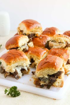 several mini sandwiches with meat and cheese on a cutting board next to some parsley