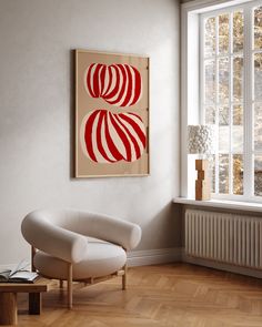 a white chair sitting in front of a window next to a painting on the wall