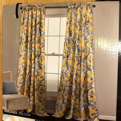 a yellow and blue floral curtain hanging in front of a window next to a chair