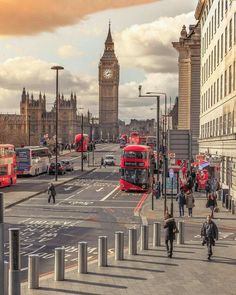 people crossing the street in london with big ben in the backgroung and red double decker buses