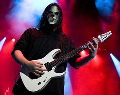 a man with long black hair and makeup playing a guitar in front of red and blue lights