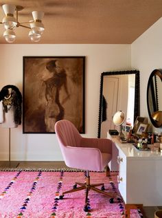 a pink chair sitting in front of a mirror on top of a dresser next to a painting