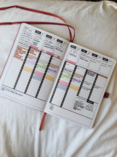 an open planner book sitting on top of a bed next to a red ribbon and pillow