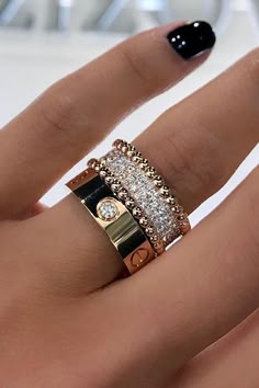 a woman's hand with black and gold rings on it, holding onto her manicured nails