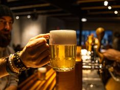 a man is holding a glass of beer in front of another man at a bar