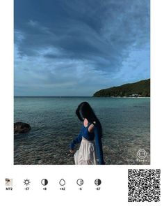 a woman standing on top of a beach next to the ocean under a cloudy sky