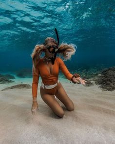 a woman in an orange bathing suit and goggles sitting on the sand under water