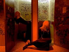 a woman sitting in a public restroom with graffiti on the walls