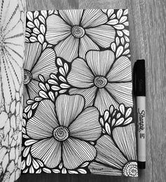 a black and white drawing of flowers next to a pen on top of a notebook