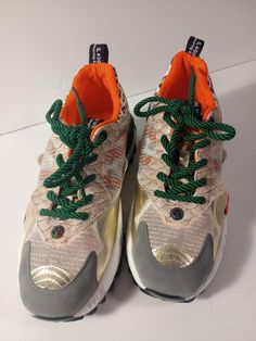 a pair of sneakers with green and orange laces on the top, sitting on a white surface