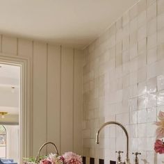 a kitchen with white tiles and pink flowers on the counter top, along with black and white tile