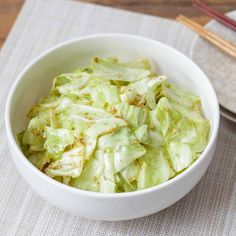 a white bowl filled with lettuce next to chopsticks on a table