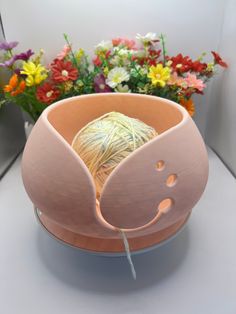 a ball of yarn sits in a vase with flowers behind it