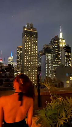 a woman standing on top of a roof in front of the city skyline at night