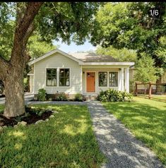 a small white house with a tree in the front yard and gravel path leading to it