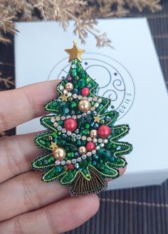 someone is holding a christmas tree brooch in their hand