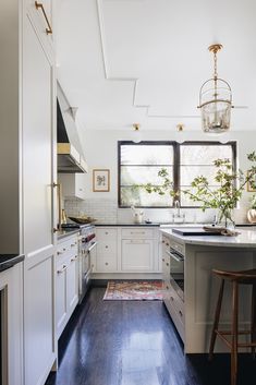 a kitchen with white cabinets and wood floors, along with a large window over the sink