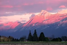 the mountains are covered in pink and purple clouds as the sun is setting on them