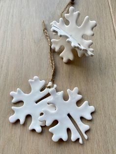 two white snowflake ornaments on a wooden table with twine cord attached to them