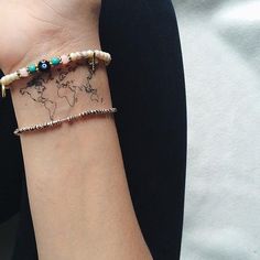 a woman's arm with a world map on it and beaded bracelets