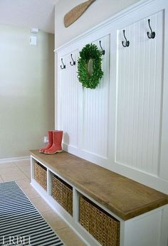 a bench with two baskets on it next to a wall mounted coat rack and hooks