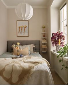 a bed sitting next to a window in a bedroom under a white light hanging from the ceiling