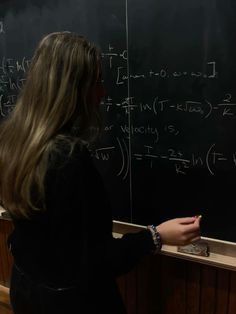 a woman standing in front of a blackboard writing on it