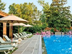 an empty swimming pool surrounded by lawn chairs and umbrellas with trees in the background