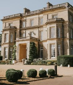 a large stone building with lots of windows and bushes in front of the entrance to it