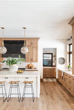 a large kitchen with wooden floors and white counter tops, along with two bar stools