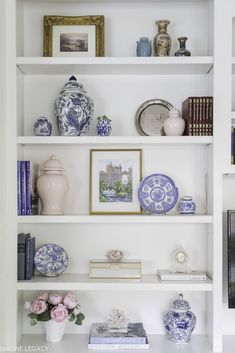 a white book shelf filled with blue and white plates, vases and other items