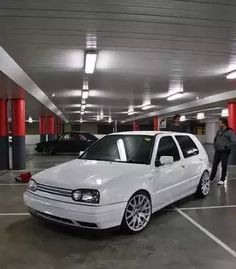 a white car parked in a parking garage with two men standing next to the cars