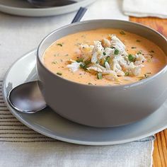 a bowl of soup is sitting on a plate with spoons and napkins next to it