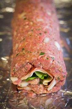 a meatloaf roll is wrapped in foil and garnished with fresh herbs