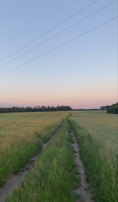 an empty dirt road in the middle of a field with power lines above it at dusk