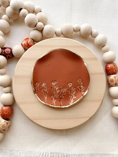 a wooden plate with flowers on it surrounded by white beads and wood bead necklaces