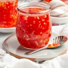 a jar filled with red sauce sitting on top of a plate next to a spoon