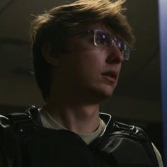 a young man wearing glasses looking off into the distance in front of a blue light