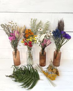 four vases filled with different types of wildflowers on a white wooden surface