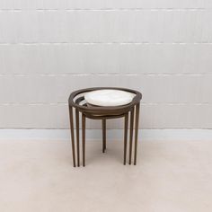 a small round table with a white cushion on it's top in front of a white brick wall