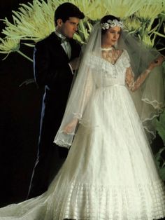 a man and woman in wedding attire standing next to each other with flowers behind them