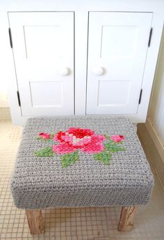 a crocheted bench with pink flowers on it in front of a cabinet and tiled floor