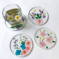 three glass coasters with flowers painted on them next to a cup and saucer