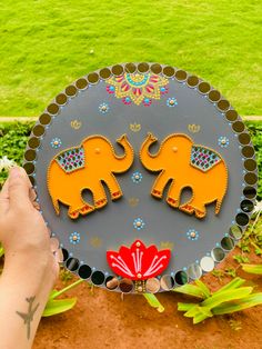 a person holding a plate with two elephants on it in front of some green grass