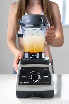 a woman is using a blender to make orange juice