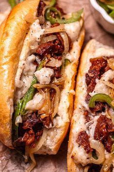 two sandwiches with meat, onions and green peppers on a table next to some dipping sauce