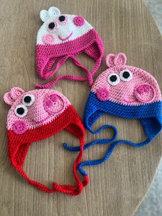 three crocheted hats with eyes and ears on top of a wooden table,