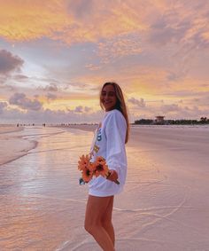 a beautiful woman standing on top of a sandy beach next to the ocean at sunset