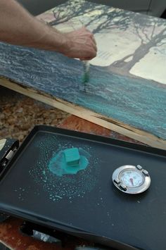 a person is using a knife to paint a piece of wood with green wax on it