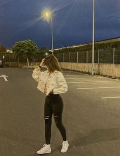 a woman standing in the middle of an empty parking lot at night talking on her cell phone